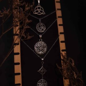 Díjes simbólicos en acero con geometría sagrada como cubo de Metatrón, flor de la vida, triqueta y nudo de bruja. Protección, equilibrio y conexión espiritual.